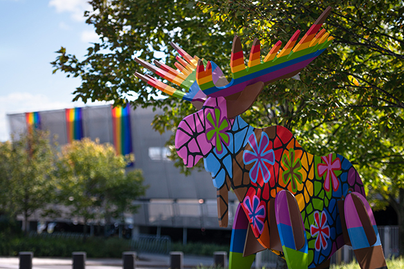 Brightly coloured wooden moose in front of Pride flags hanging on the side of a building