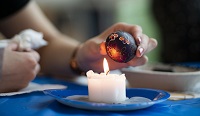 A hand holds a dyed Ukrainian Easter egg above a candle flame